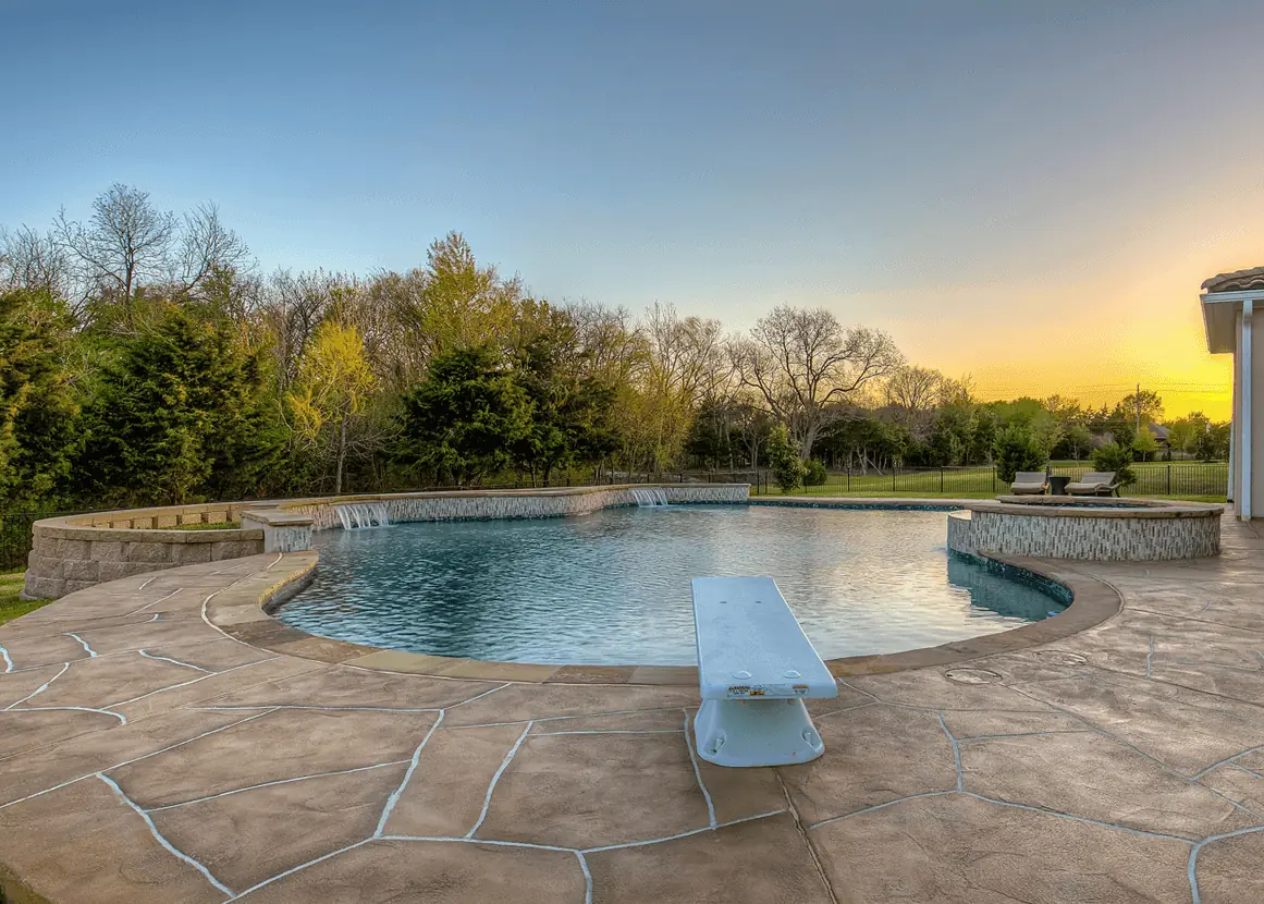Freeform pool with raised stone walls, water spillways and a raised spa at sunset