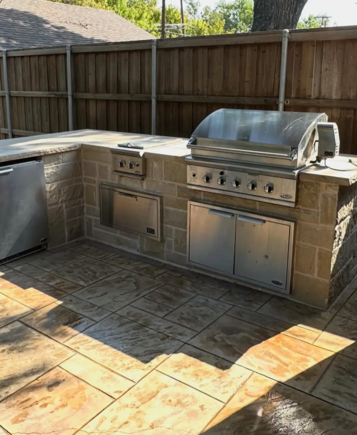 Stone outdoor kitchen with a stainless built-in grill, side burner and storage doors on a stamped concrete patio